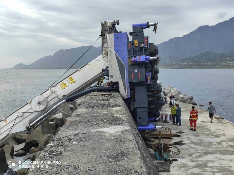 台東成功漁港30日中午一輛吊車在碼頭吊掛消波塊時不慎翻覆，吊臂卡進海中消波塊間，車體翻覆堤防，車內2人受困，警消獲報到場1人OHCA，1人經器材破壞後獲救送醫。（民眾提供）中央社記者李先鳳傳真　114年11月30日